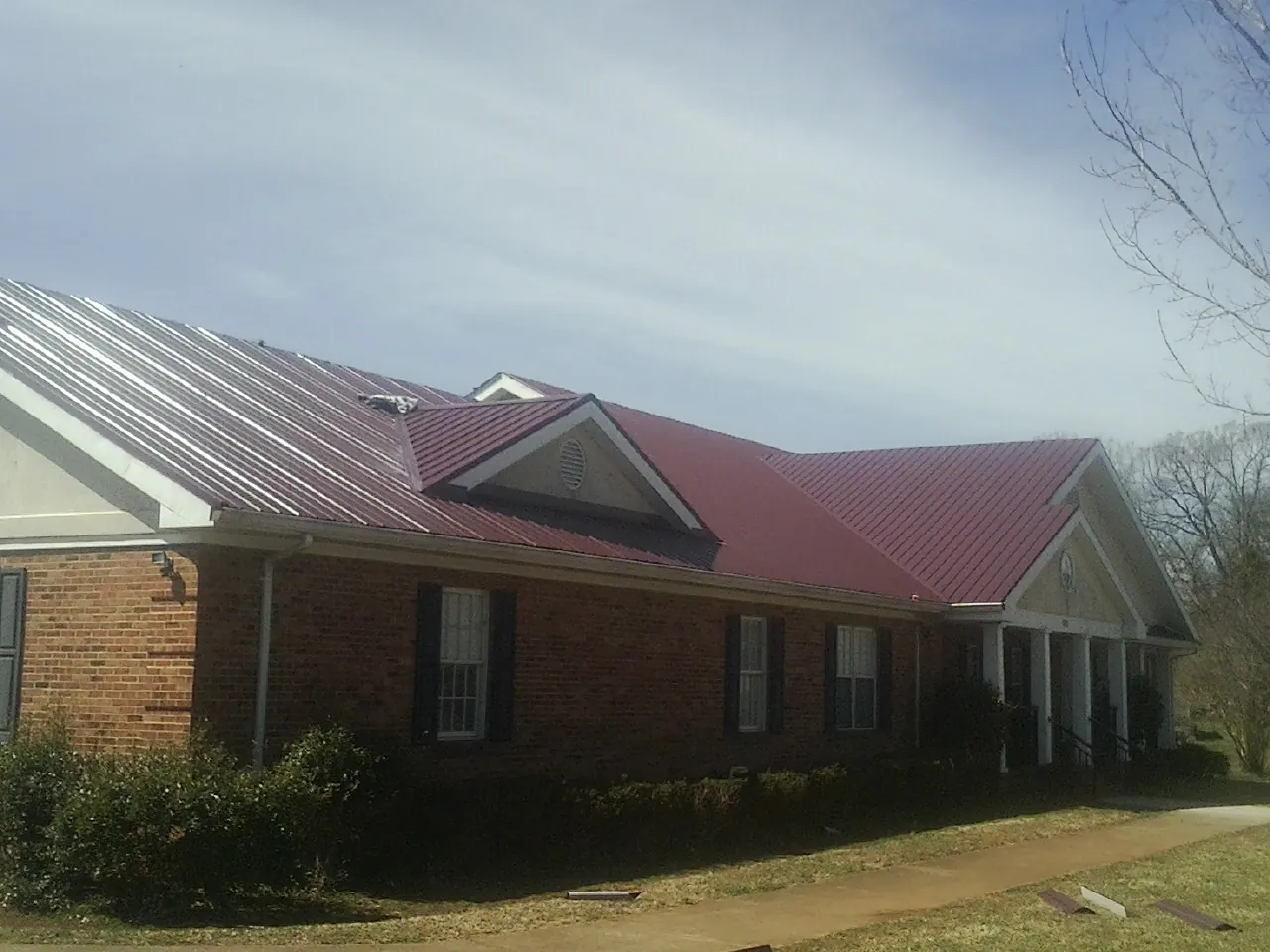 Red metal roof with gabled entries on a long brick building, from a Hail Damage Roof Repair job in Adams