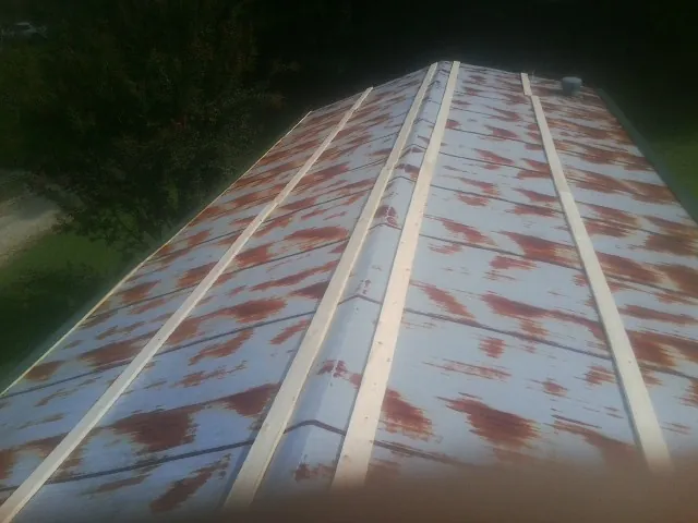 Rusted metal roof panels with new wood purlins before replacement in Adams
